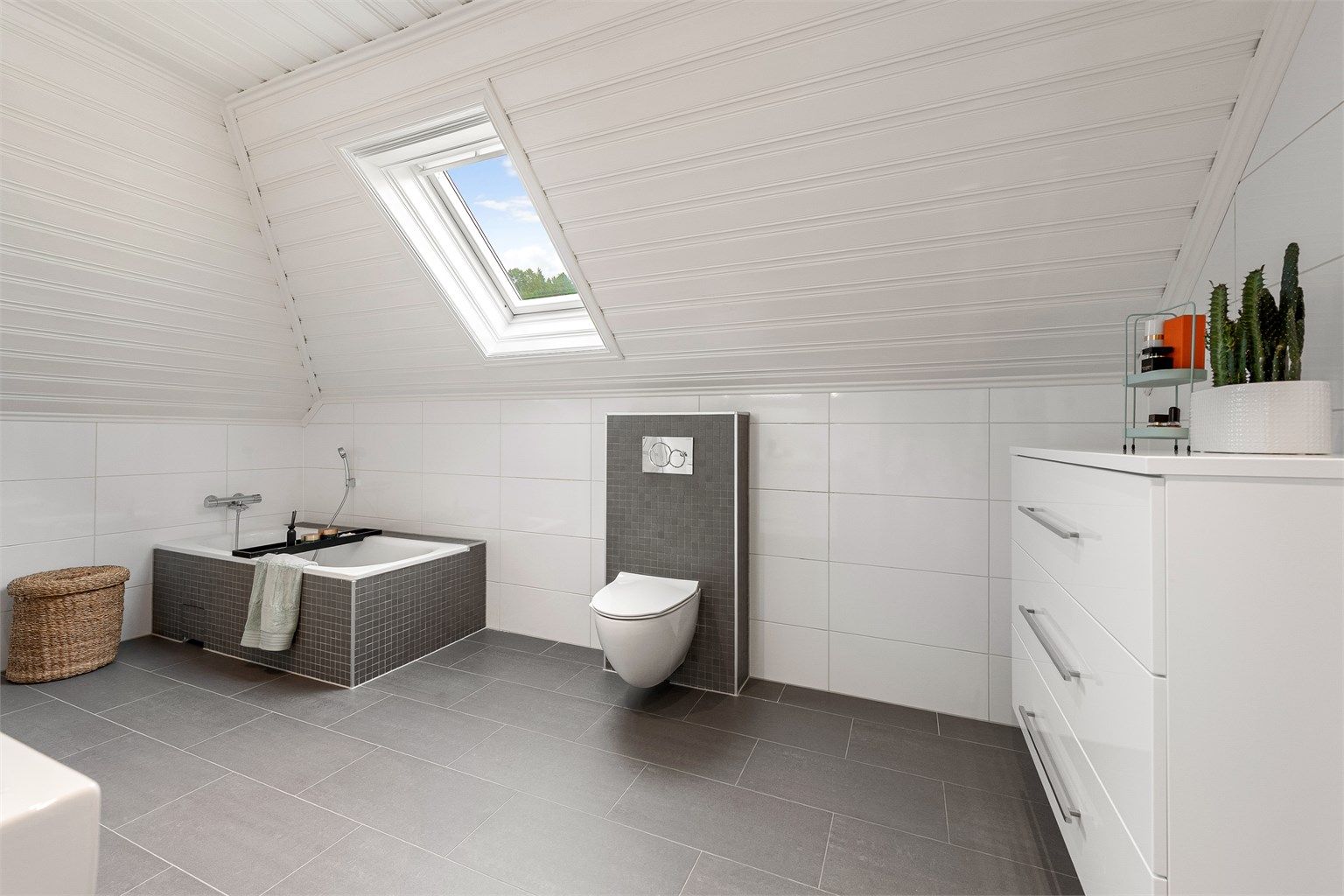 Badet på loft har innebygget badekar og vegghengt toalett. Gode lysforhold fra takvindu.