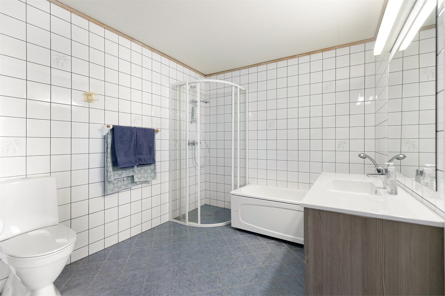 Badet i underetasjen har varmekabler, badekar med dusjløsning, toalett og servant.