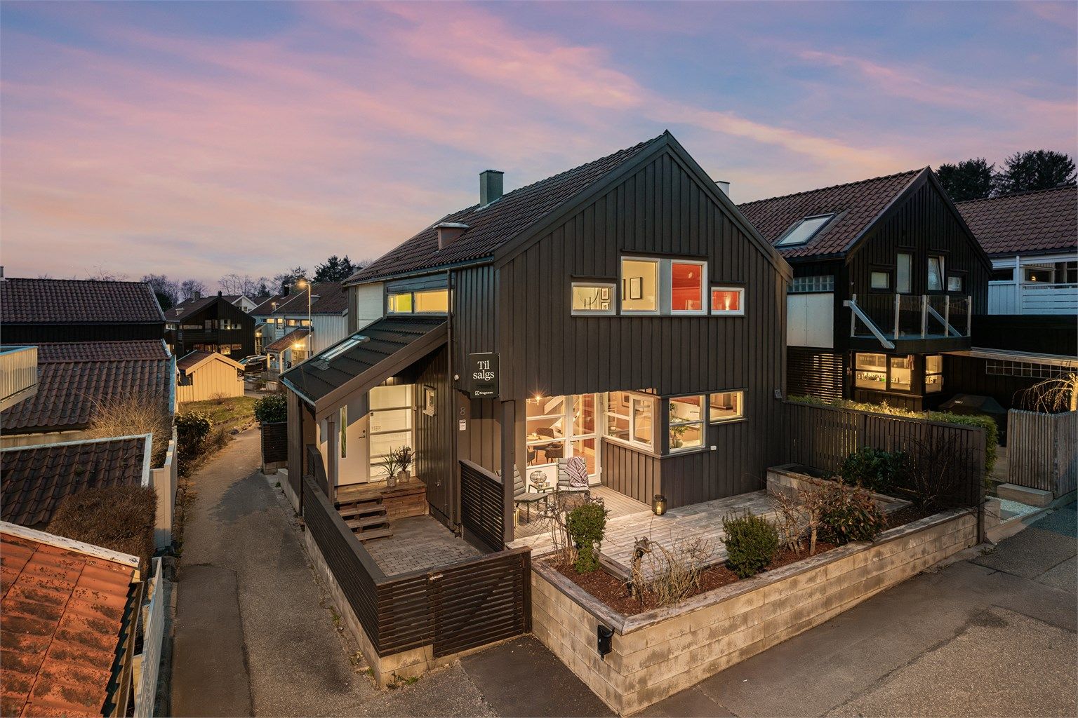 Parkering på felles område foran inngangsparti. Her er det montert el-bil lader. Terrasse ved inngangsparti. 