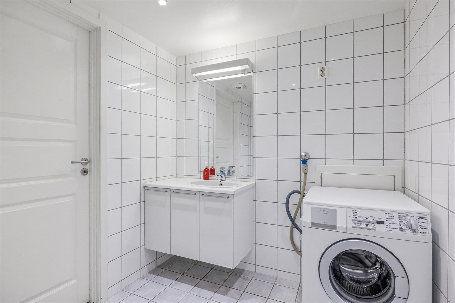 Det er vegghengt servantskap med nedfelt servant og speil med overlys. Vaskemaskin kan følge