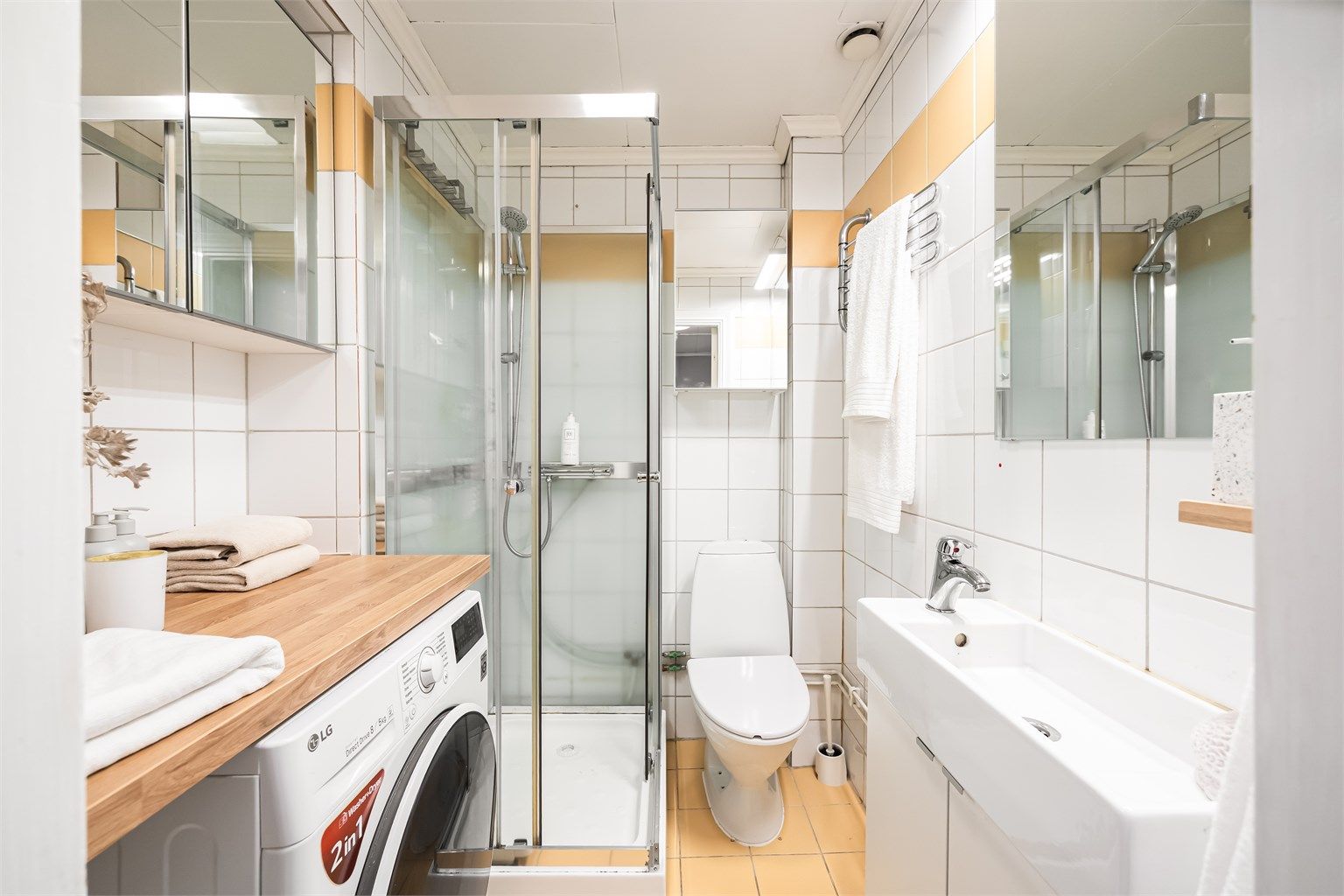 Flislagt bad med varmekabler i gulv, innredet med vegghengt servantinnredning med ovenpåliggende vask, dusjkabinett og gulvstående klosett.