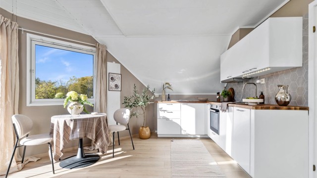 Kjøkkenet fra 2023 har hvite, glatte fronter og benkeplate i laminat.