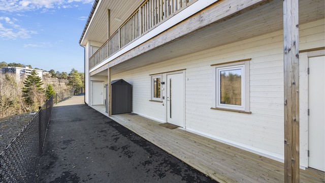 Fin uteplass ved inngangspartiet med takoverbygg og asfaltert vei.