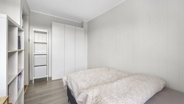 Et av etasjens tre soverom, med laminat på gulv og malte panelplater på vegg.