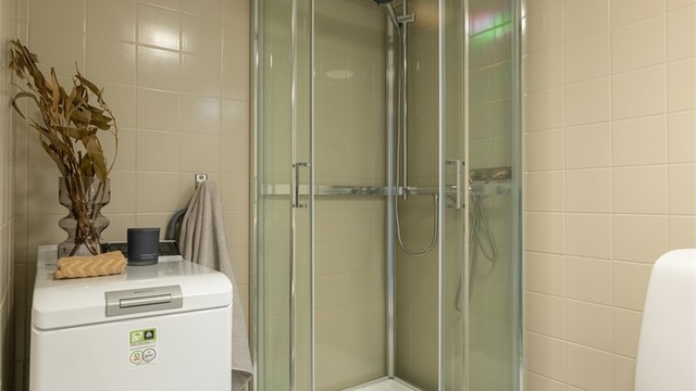 Lyst og flislagt bad med varmekabler i gulv og opplegg for vaskemaskin. Dusjkabinett med skyvedører i glass.