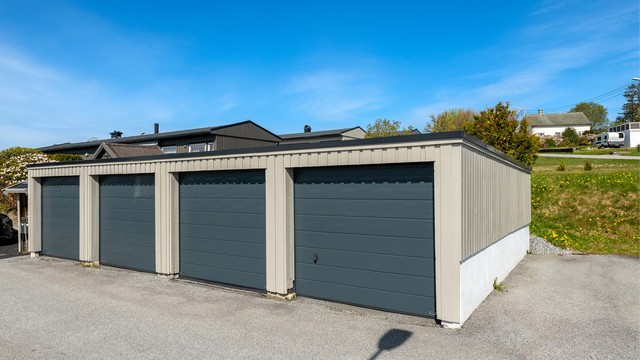Garasjeplass i felles anlegg med ny leddport i metall og nylig installert ladepunkt for elbil