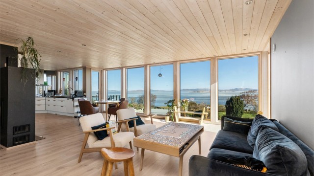 De brede vinduene fra gulv til tak gir en sømløs overgang mellom stuen og det omkringliggende kystlandskapet.
Foto: Marianne Lyse.