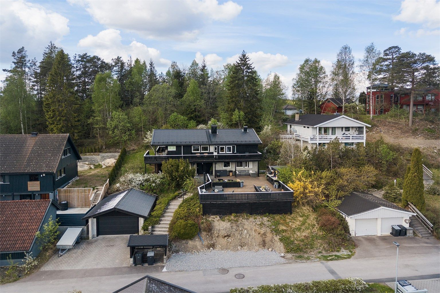 Eiendommen ligger i skrånende terreng med opparbeidet hage og plenarealer.