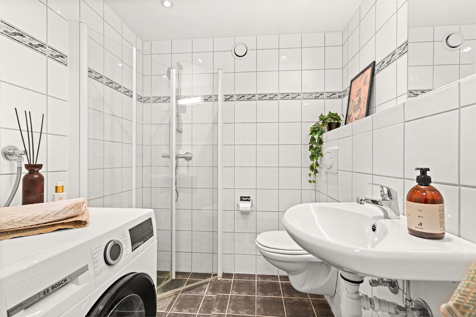 Flislagt bad med lyse overflater, praktisk dusjhjørne og servant. 