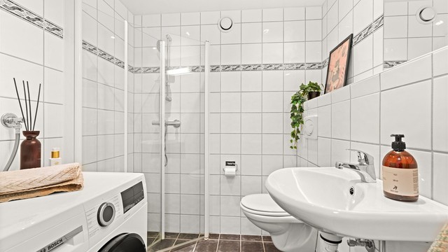 Flislagt bad med lyse overflater, praktisk dusjhjørne og servant.