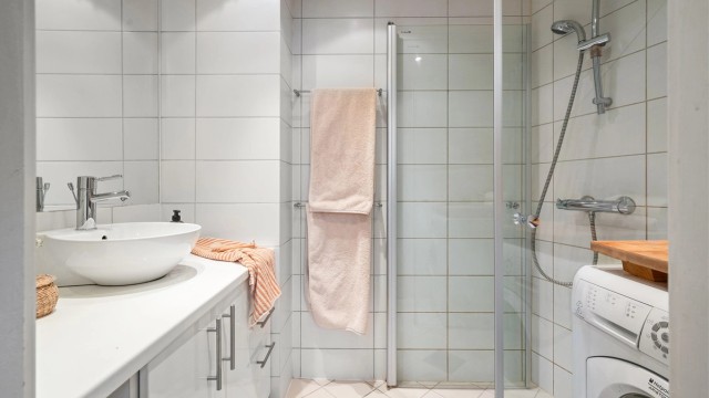 Pent flislagt bad som har dusjhjørne med innfellbare dører, veggmontert servantinnredning med slette fronter og speil med overlys.