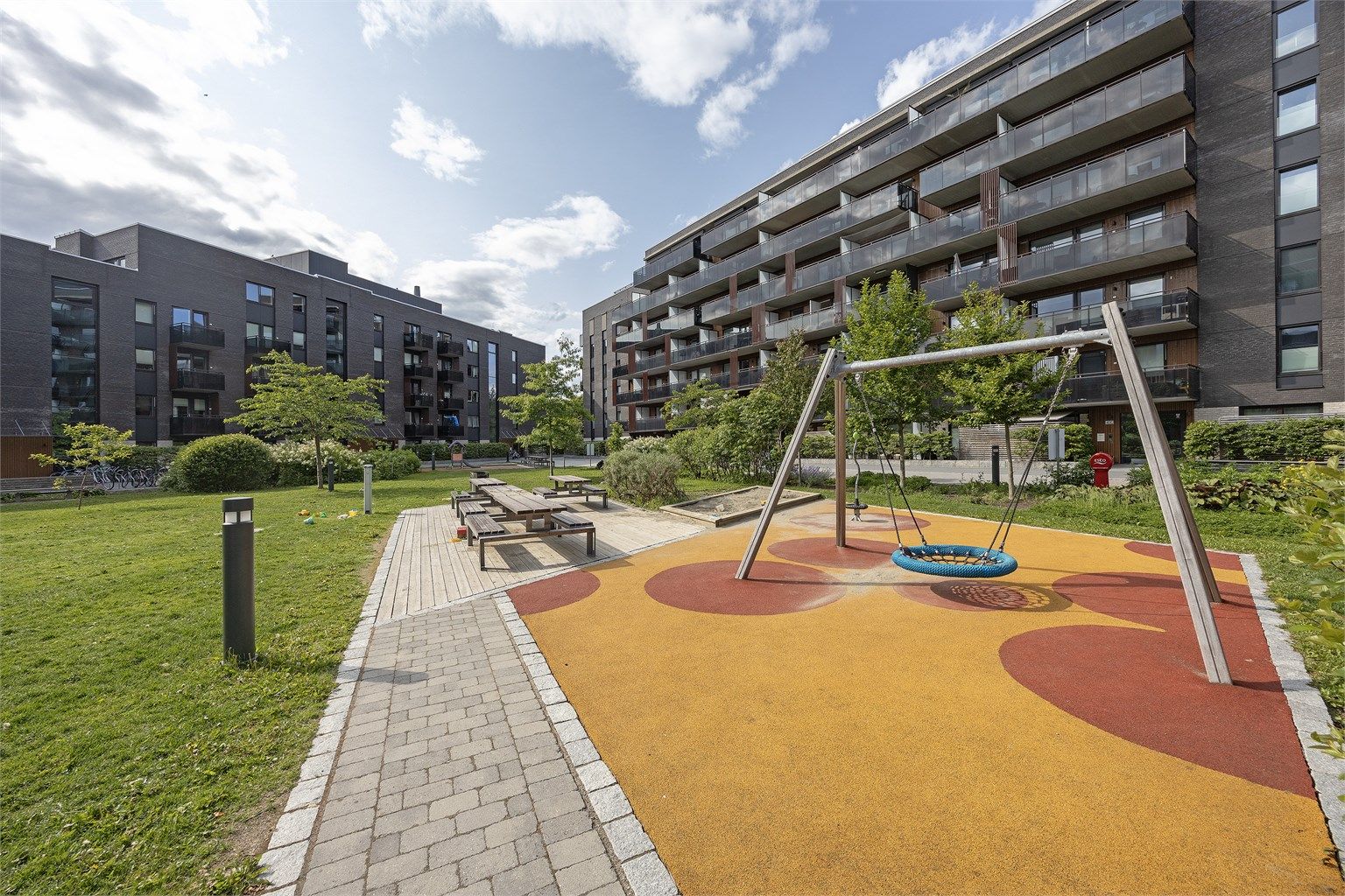 Nydelig felles indre gårdsrom med lekeapparater, sittebenker og grill, sykkelparkering, asfalterte lysbelagte stier og grønne områder med gressplen, prydbusker, trær og diverse beplantning