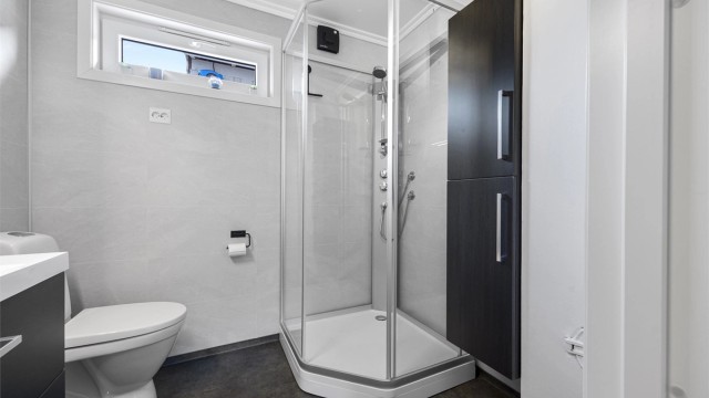 Badet er utstyrt med dusjkabinett, vegghengt toalett og servant med skuffeseksjon.