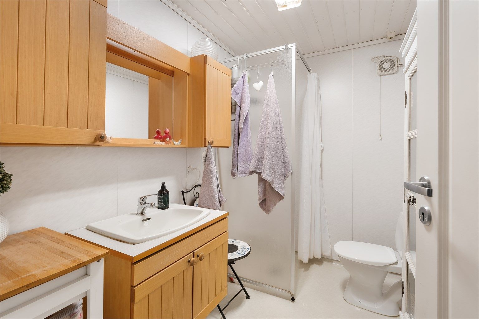 Badet er innredet med baderomsplater på vegger, belegg på gulv og panel i himling. Dusjnisje med forheng. Innredning med profilerte fronter og laminert benkeplate