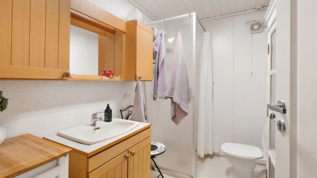 Badet er innredet med baderomsplater på vegger, belegg på gulv og panel i himling. Dusjnisje med forheng. Innredning med profilerte fronter og laminert benkeplate