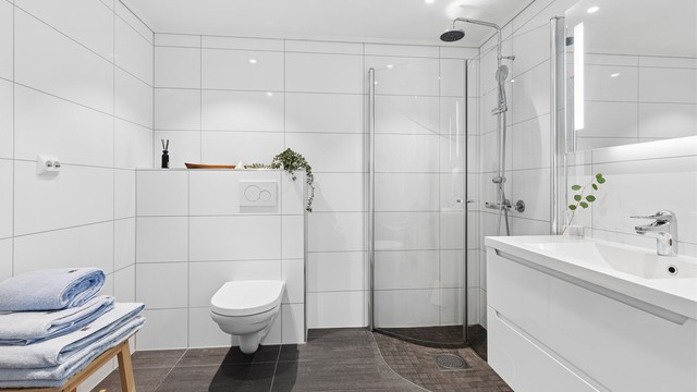 Badet i 1.etg har moderne lekre fliser, gulvvarme, vegghengt toalett og servantskap med god plass samt dusjhjørnet med praktiske innfellbare dører.