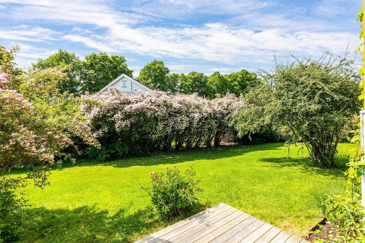 Fra plattingen kan du gå rett ut i borettslagets vakre hage med stor gressplen og blomstrende prydbusker.