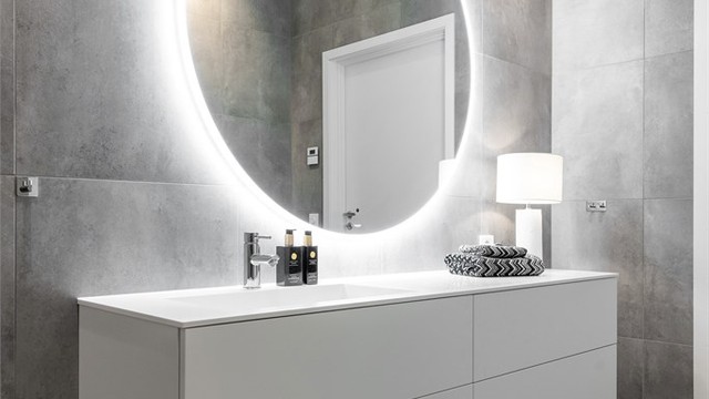 Stor romslig baderomsinnredning fra Azzurro med hvite glatte fronter og nedfelt vask med ett-greps armatur. Rundt speil med lys og stikkontakter over servant.