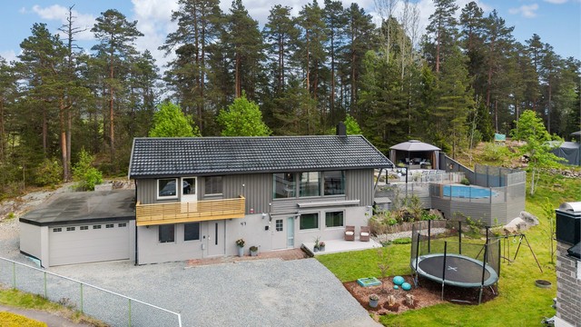 Romslig, singelbelagt gårdsplass med tilliggende garasje + bod. Elbillader er montert på husvegg.