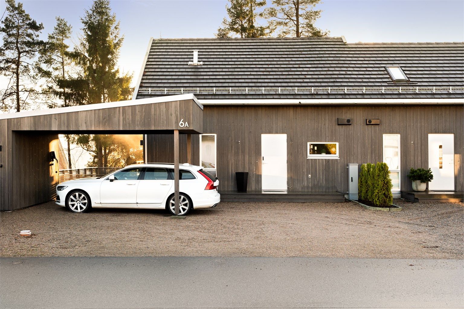 Moderne trefasade med skråtak og integrert carport som gir rene linjer, og innbydende ankomst.