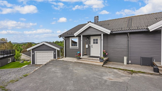 Asfaltert gårdsplass med parkering foran boligen og garasjen.