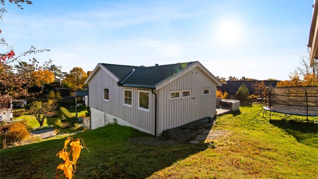 Skrånende tomt opparbeidet med plen, fjellknauser og beplantning.