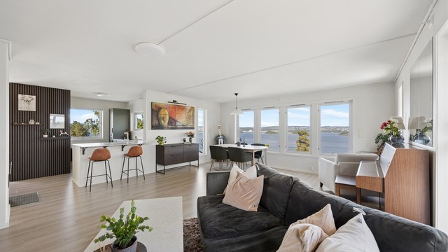 Fra stuen nyter du panoramautsikt over Oslofjorden, Nesoddlandet og helt inn til Oslo sentrum. Den åpne løsningen mellom stue og kjøkken gir et sosialt og innbydende oppholdsrom med meget gode lysforhold.