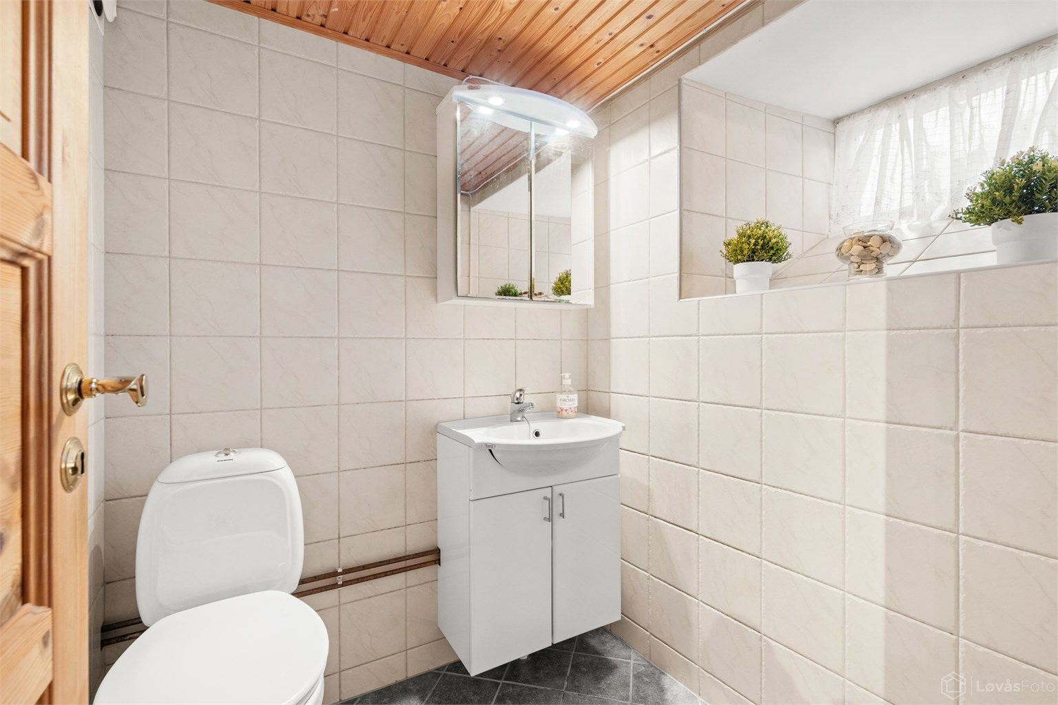 Praktisk toalettrom i kjelleren med flislagt gulv med elektrisk gulvvarme og vegghengt servantskap.