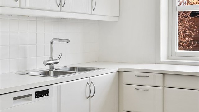 Kjøkkeninnredningen har laminert benkeplate, nedfelt vask og fliser over benken.