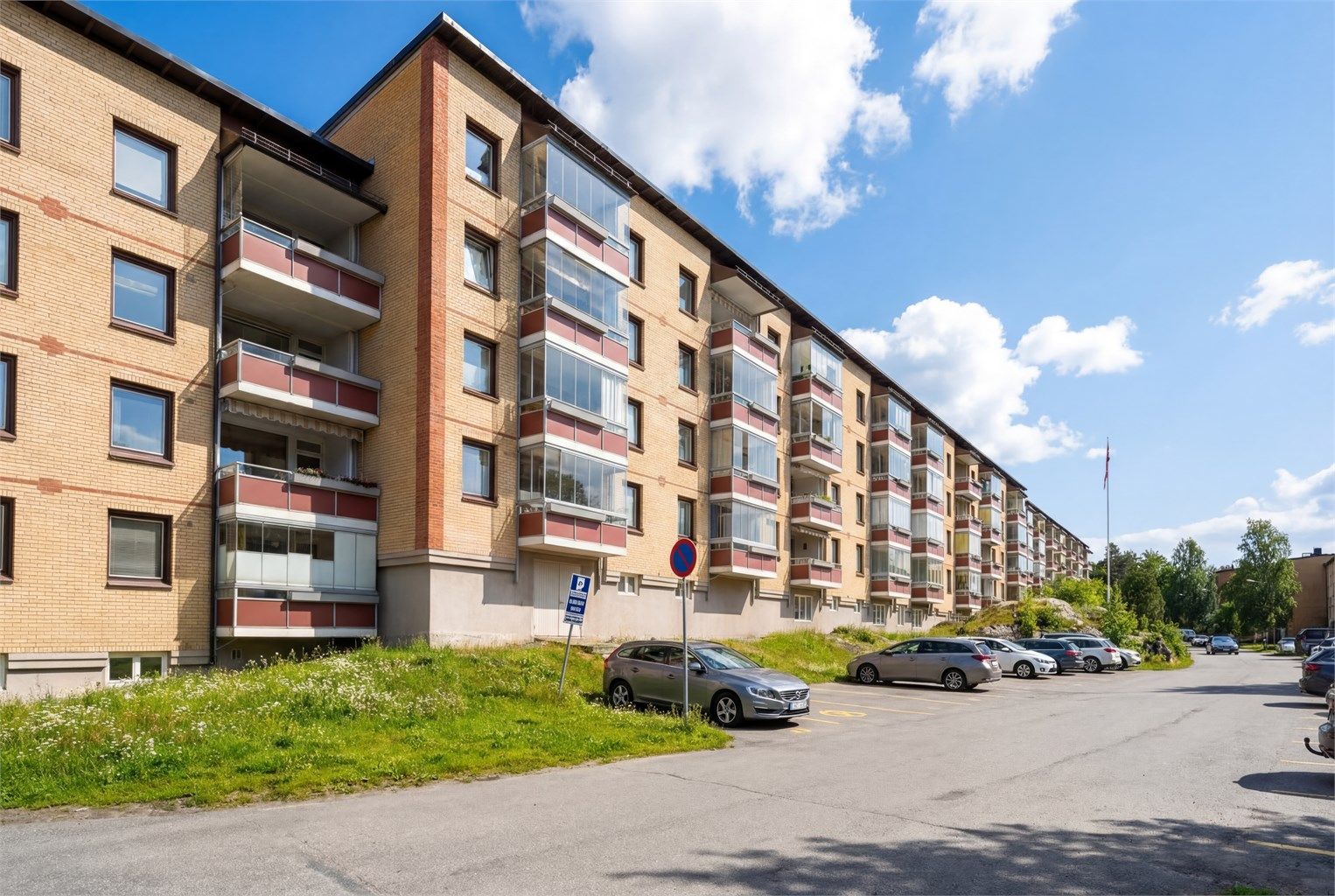 Fasaden sett fra balkong siden, sommerstid. 
Borettslaget tilbyr parkeringsplasser etter venteliste, og det er tilgang til elbillading.