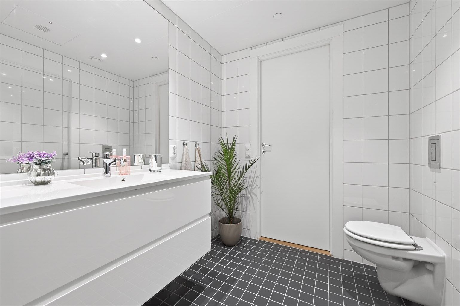 Videre er badet innredet med servant med speil og sideskap, vegghengt toalett og dusjhjørne.