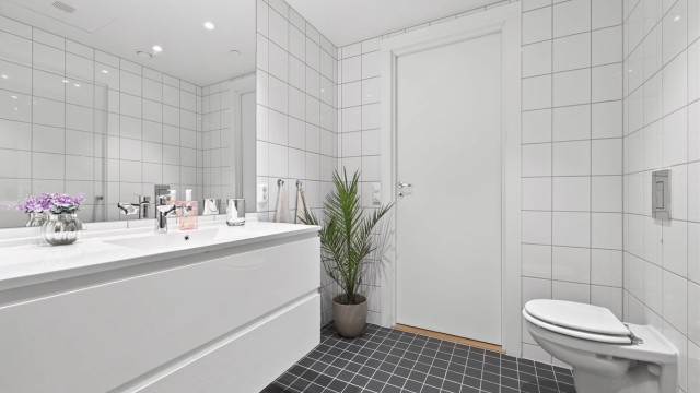 Videre er badet innredet med servant med speil og sideskap, vegghengt toalett og dusjhjørne.