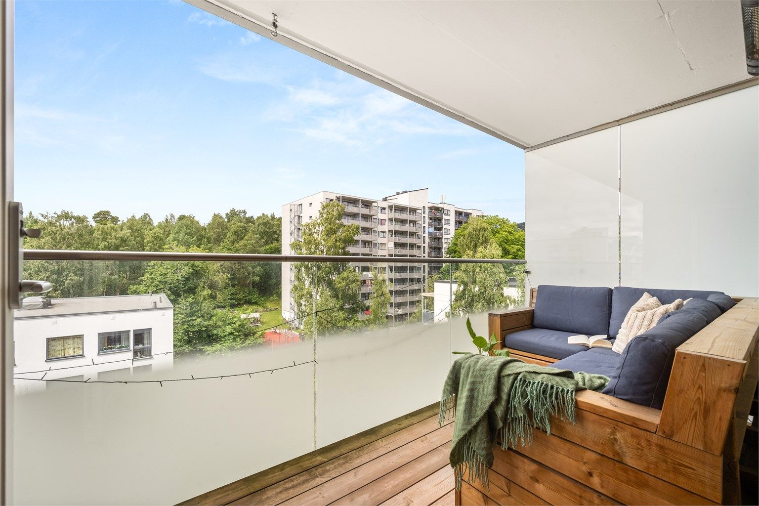 Balkongen har gulv belagt med terrassebord og et moderne rekkverk av metall og glass.