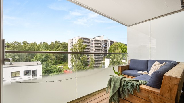 Balkongen har gulv belagt med terrassebord og et moderne rekkverk av metall og glass.