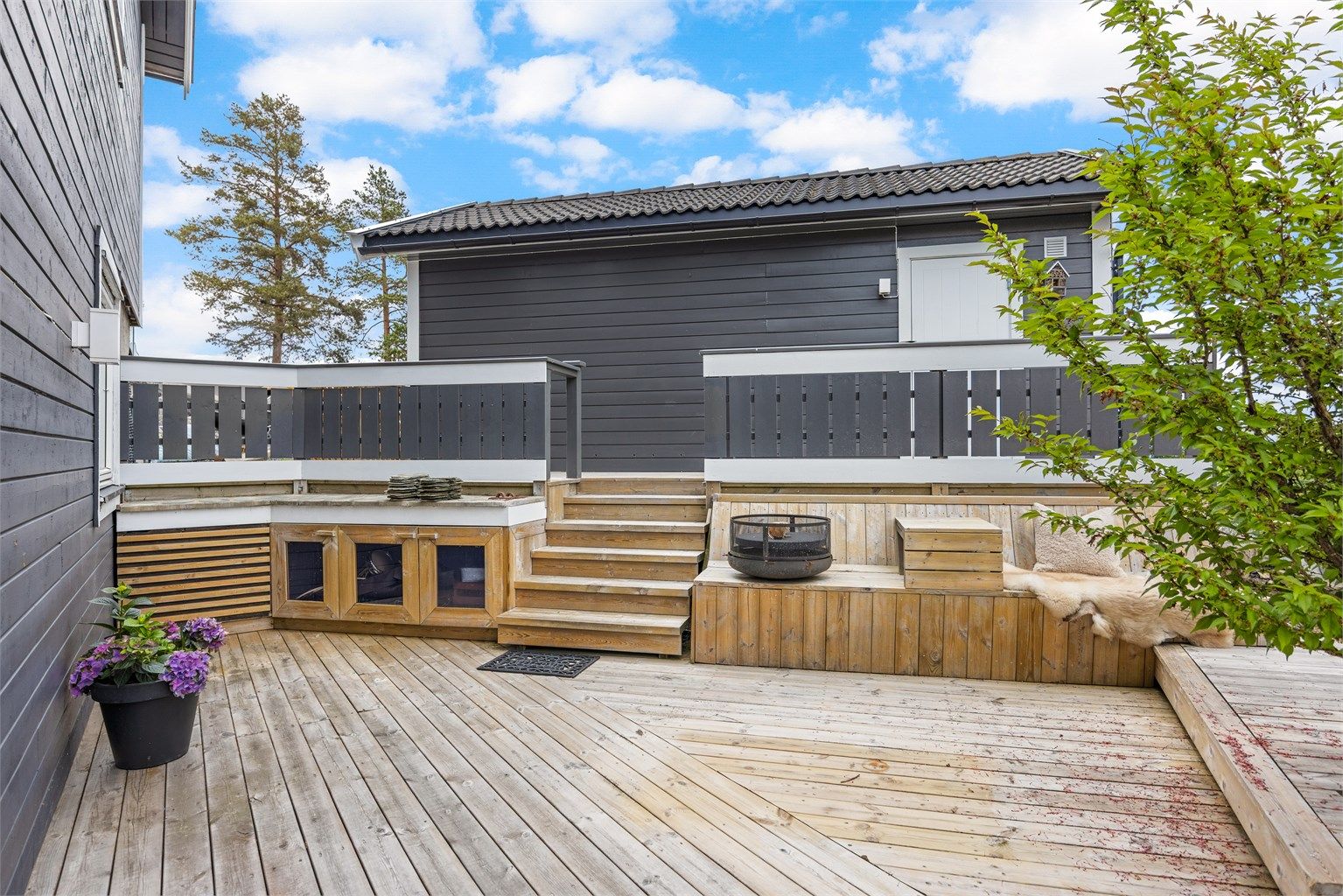 Uteområdet er anlagt med flere nivåer og soner, inkludert en plassbygd sittebenk og bålpanne.
