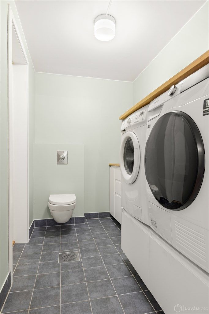 Praktisk vaskerom med flislagt gulv med gulvvarme, opplegg for vaskemaskin og tørketrommel.
