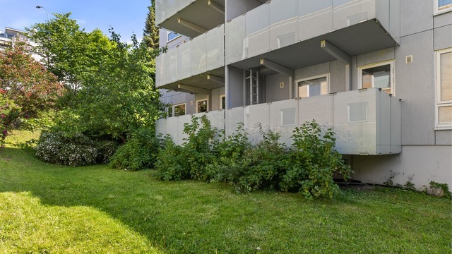 Bygget ligger tilbaketrukket i et etablert og velholdt boligmiljø, omgitt av grønne uteområder.