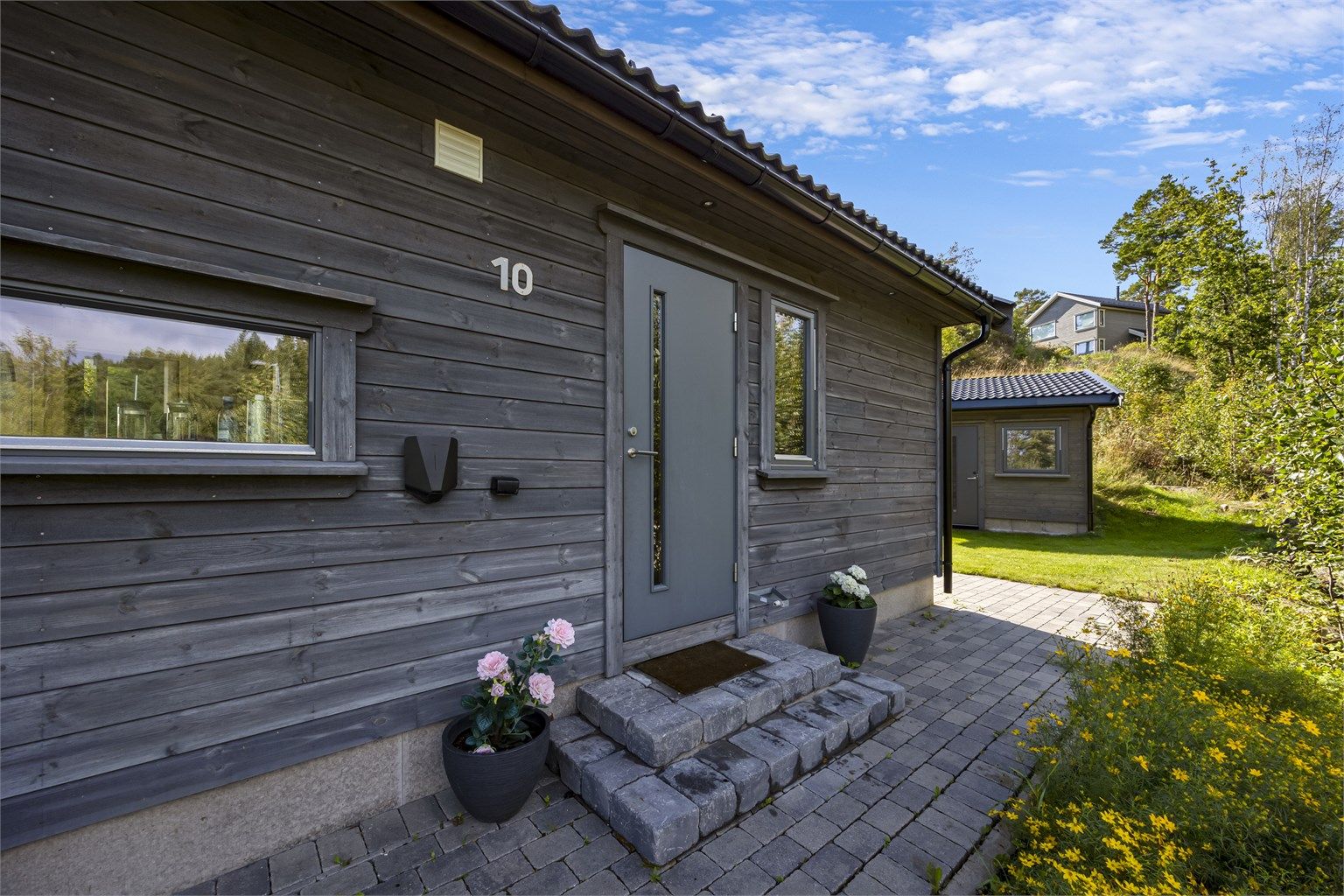 Et velholdt inngangsparti med belegningsstein og elbillader.