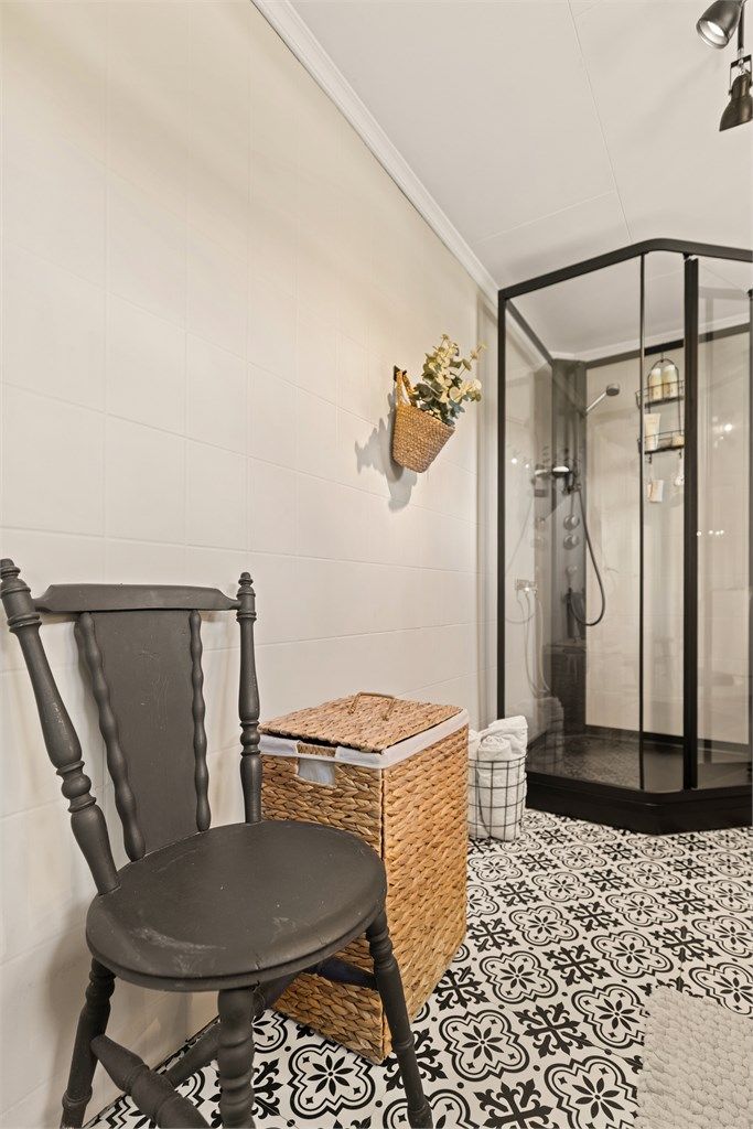 Badet har mønstrede gulvfliser og dusjkabinett med sorte profiler.