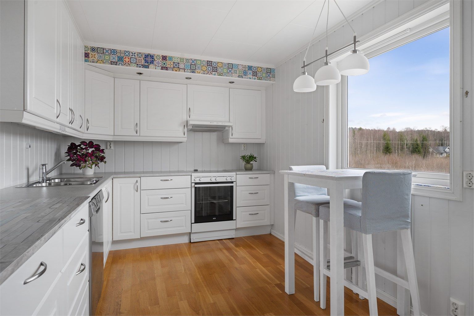 Kjøkkeninnredningen har hvite, profilerte fronter, laminert benkeplate og en praktisk frokostplass ved vinduet.