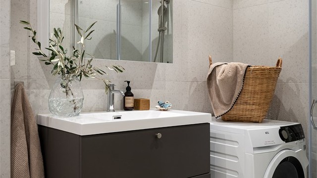 Badet er utstyrt med vegghengt toalett, dusjsone med glassvegger, servant med innredning og opplegg for vaskemaskin.