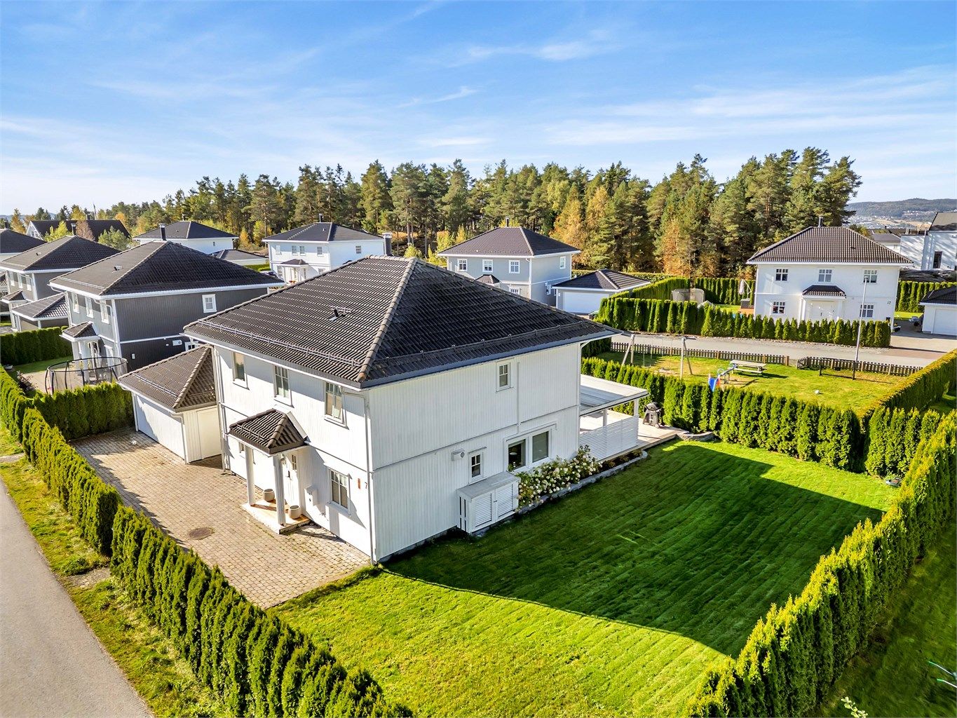 Eiendommen har en pent opparbeidet tomt med frodig plen, prydbusker og variert beplantning som rammer inn eiendommen på en elegant måte.