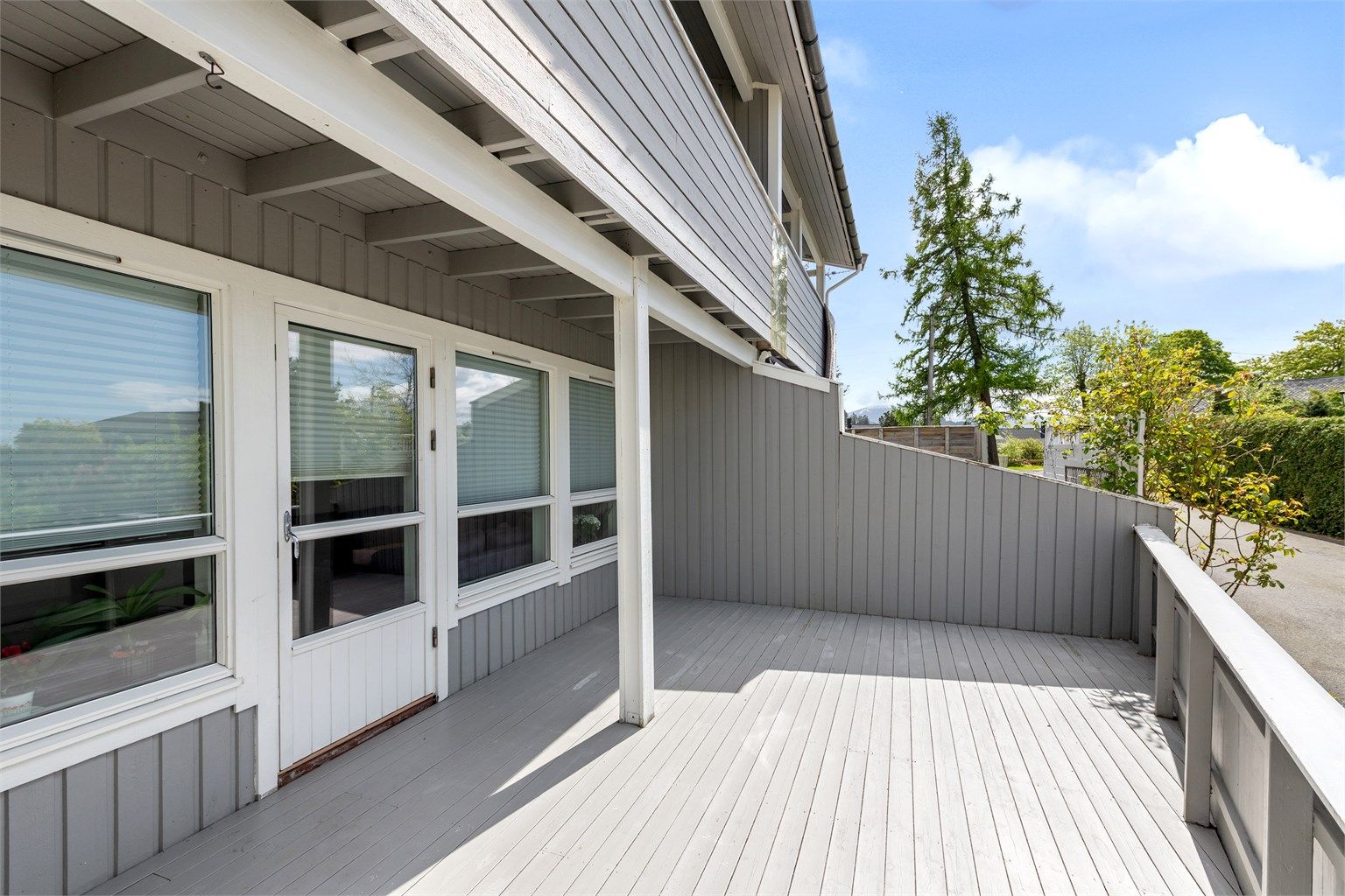 Stor markterrasse på terrens skjermet med rekkverk og levegg mot nabo