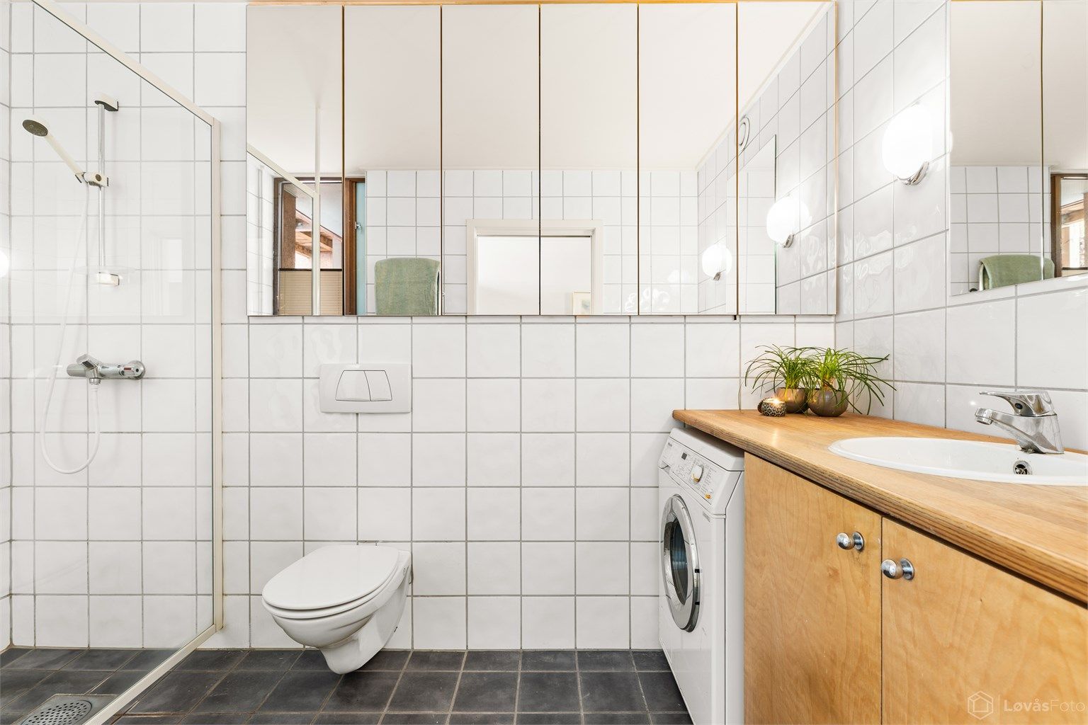 Badet er flislagt og utstyrt med vegghengt toalett, dusjhjørne og opplegg for vaskemaskin.
