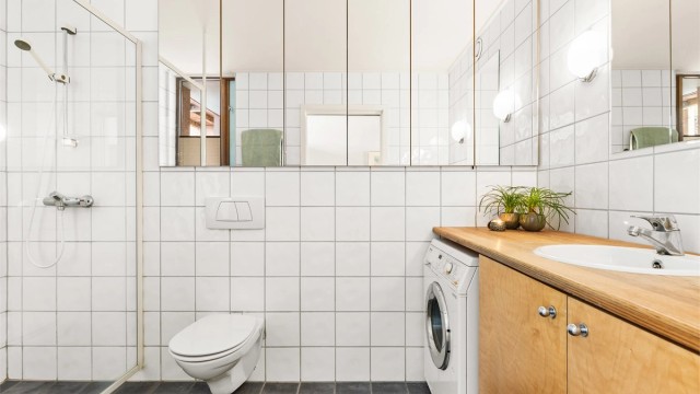 Badet er flislagt og utstyrt med vegghengt toalett, dusjhjørne og opplegg for vaskemaskin.