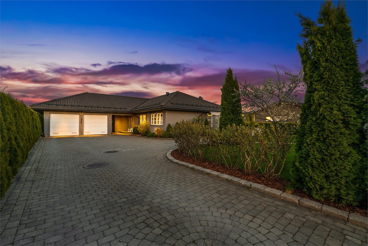 Steinbelagt gårdsplass med parkering i dobbeltgarasje, parkmessig opparbeidet og lettstelt hage. 