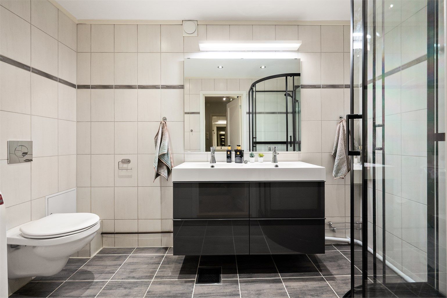Badet har varmekabler og fliser på gulv og vegger. Dobbel servant gjør det mulig for to personer å benytte badet samtidig.