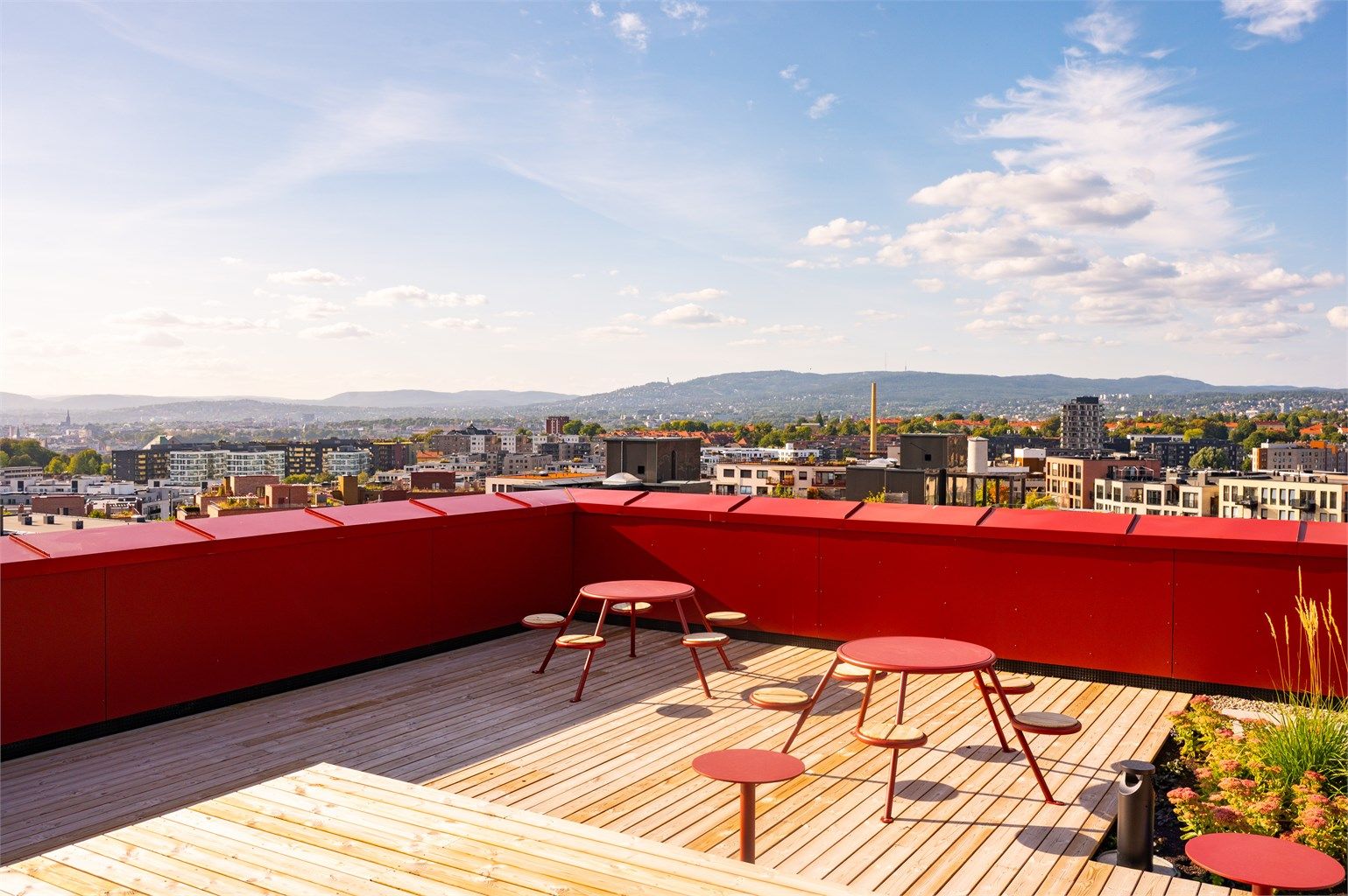 Felles takterrasse på toppen av bygget med sitteplasser og vidstrakt utsikt over byen og åsene.