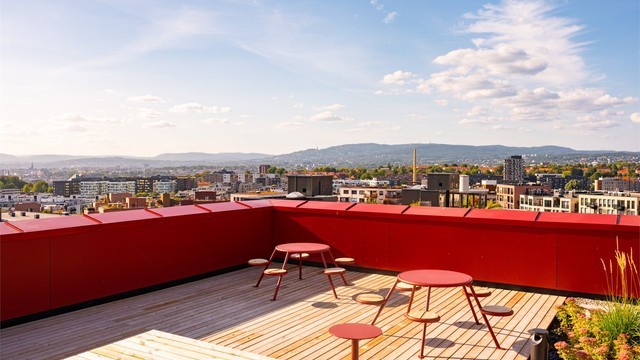 Felles takterrasse på toppen av bygget med sitteplasser og vidstrakt utsikt over byen og åsene.