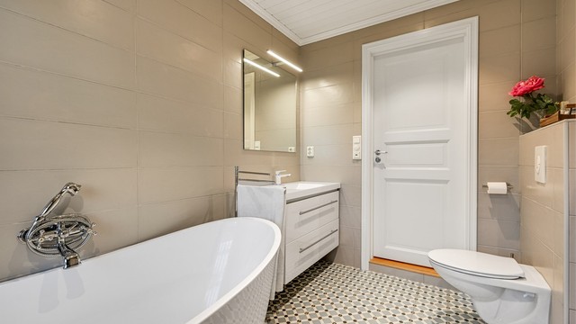 Badet har flislagte vegger, vegghengt toalett og servantmøbel med skuffer.